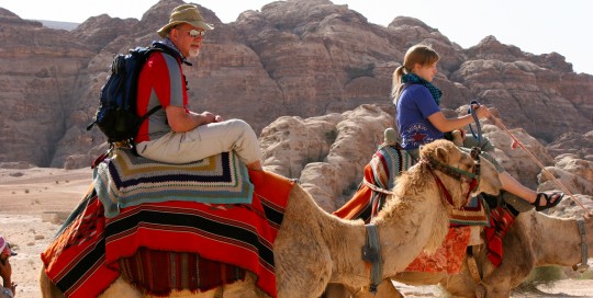 2 American guests of Engaging Cultures Travel riding camels on a Jordan tour