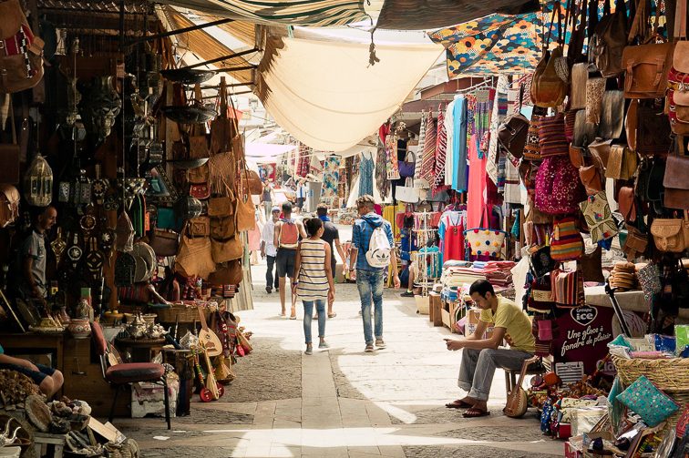 Travelers in the Tunis Medina walk on a narrow street in a colorful bazaar